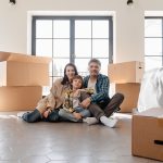 A family sitting on the floor surrounded by moving boxes